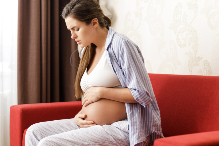 Pregnant lady sitting on sofa holding tummy