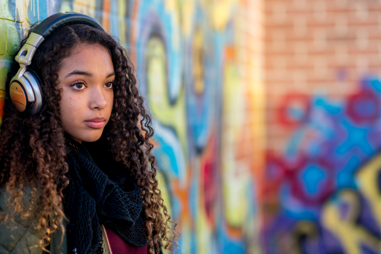 Teenage girl with headphones on leaning against wall