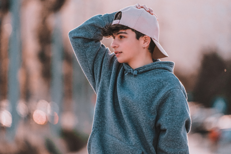 Teenage boy with grey hoodie on and baseball cap with his hand on his head