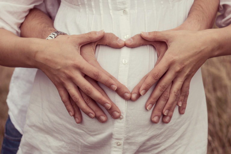 Pregnant women's stomach with couple's hands touching tummy making heart shape